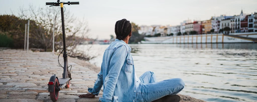 Mann sitzt am Wasser mit seinem E-Scooter