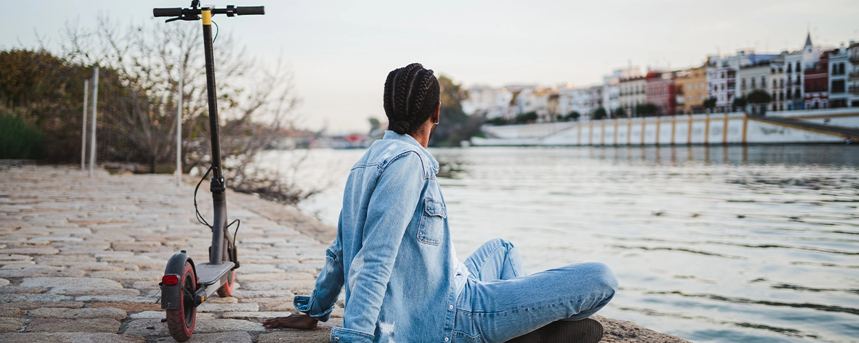 Mann sitzt am Wasser mit seinem E-Scooter
