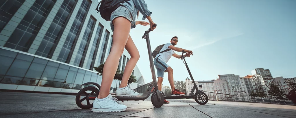 Zwei Personen auf E Scootern vor einem großen Gebäude