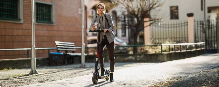 Junge Frau auf E-Scooter mit Kaffee.